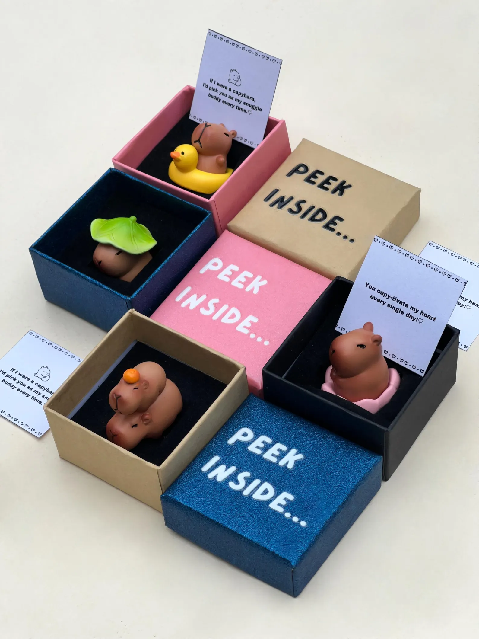 A small capybara figurine nestled inside a colorful gift box, displayed next to a poem card