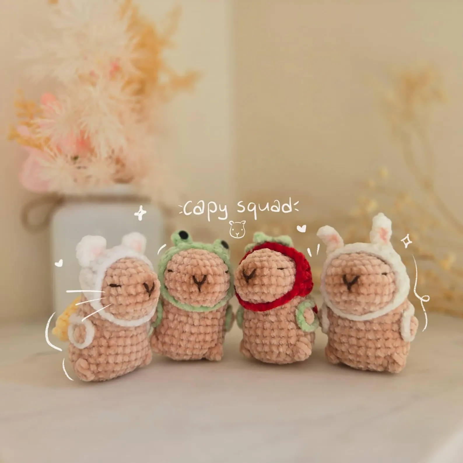 crocheted capybara keychain in beige yarn holding a tiny bag and wearing a small hat